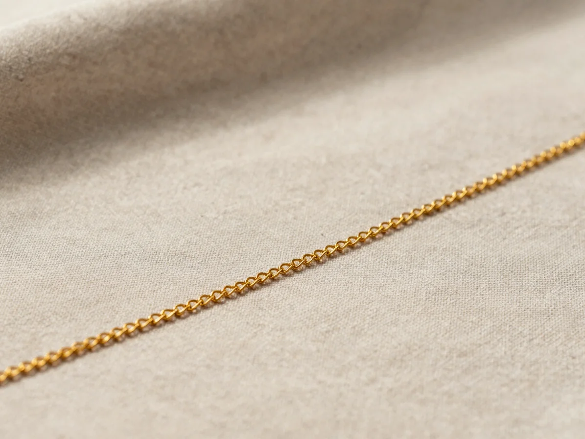 Close up of a fine gold chain resting gracefully on neutral linen fabric, soft natural lighting.